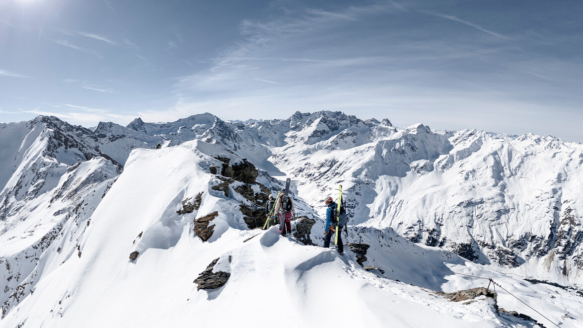 Skifahrergruppe auf verschneitem Gipfel mit Blick ins Tal / Ski group on snowy summit overlooking valley