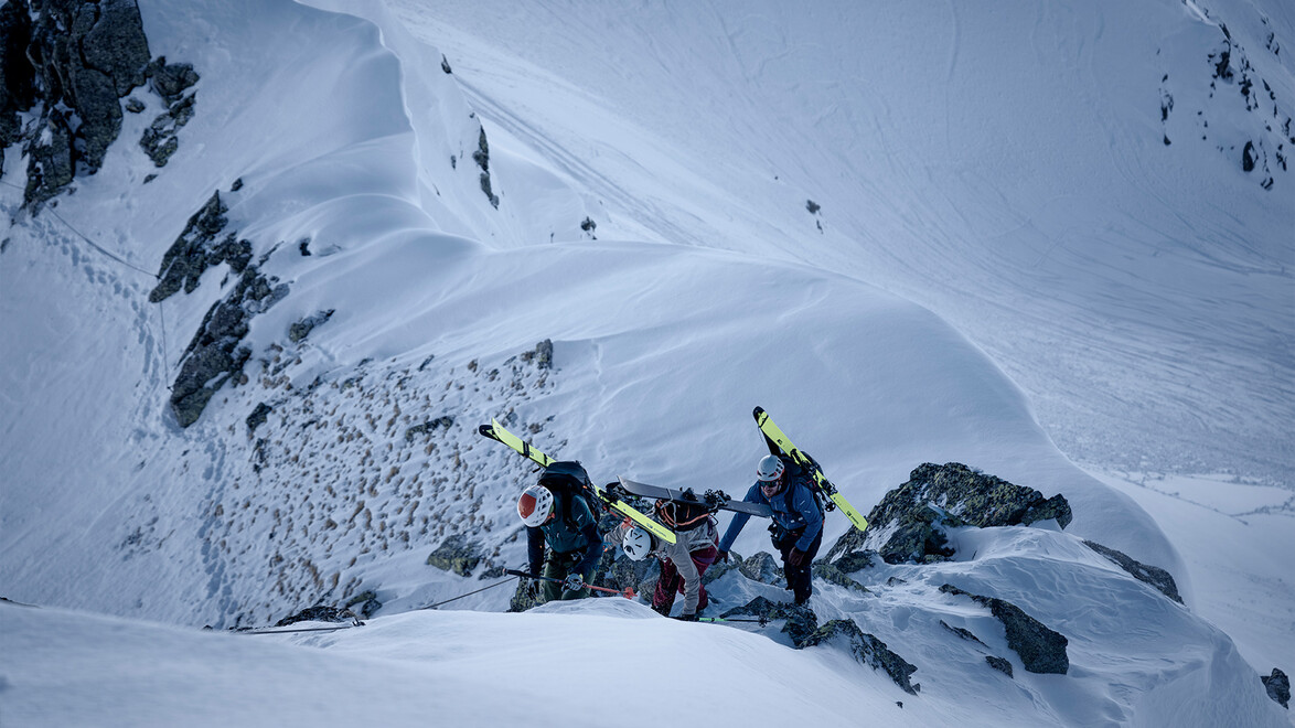 Gruppe quert steiles Schneefeld zwischen Felsformationen / Group crossing steep snowfield between rocks