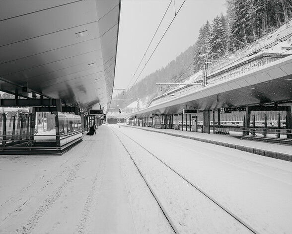 The St. Anton am Arlberg train station lies quiet and snow-covered in winter, with modern roofs, empty platforms, and snow-covered tracks.