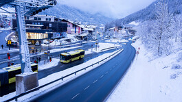 Zwei Linienbusse fahren durch das verschneite Terminal West mit Seilbahnstation in St. Anton.