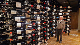 Ein Mann steht vor einem edlen Weinkeller mit vielen horizontal gelagerten Flaschen.