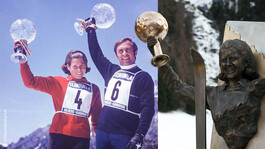 Gertrud Gabl und Franz Klammer mit Kristallkugeln und Statue von Gertrud Gabl mit Trophäe vor Bergkulisse.