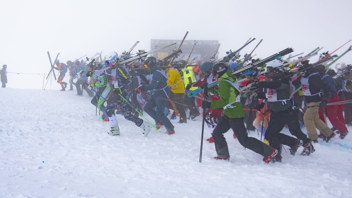 Teilnehmende starten laufend mit Skiern in der Hand bei dichtem Nebel / Participants start running with skis in hand through dense fog