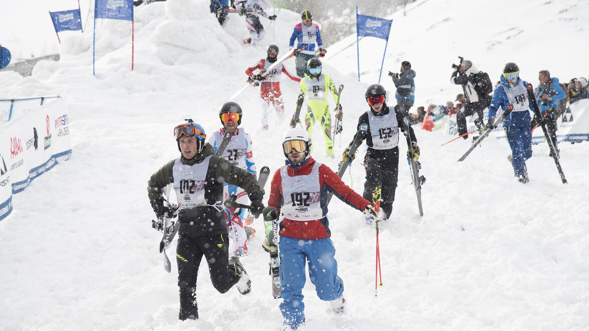 Sportlerinnen und Sportler tragen Skier über Hindernisparcours / Athletes carry skis across obstacle course