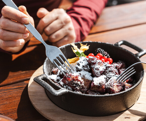 Frischer Kaiserschmarrn mit Puderzucker und Beeren wird in einer gusseisernen Pfanne serviert. Mehrere Gabeln greifen zu – ein kulinarisches Highlight auf der Berghütte.