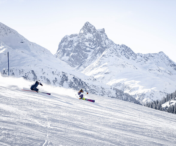 Zwei Skifahrer in sportlicher Kurvenlage vor dem markanten Gipfel des Patteriol im Skigebiet St. Anton.