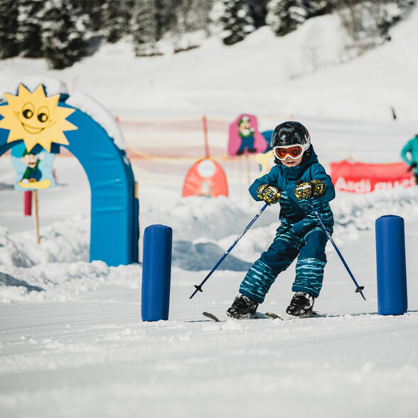 Child skiing through colorful obstacle course in snow during ski school.