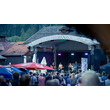 Besucher stehen vor einer Bühne, auf der eine Band bei einem Open-Air-Konzert auftritt / Visitors stand in front of a stage where a band performs at an open-air concert