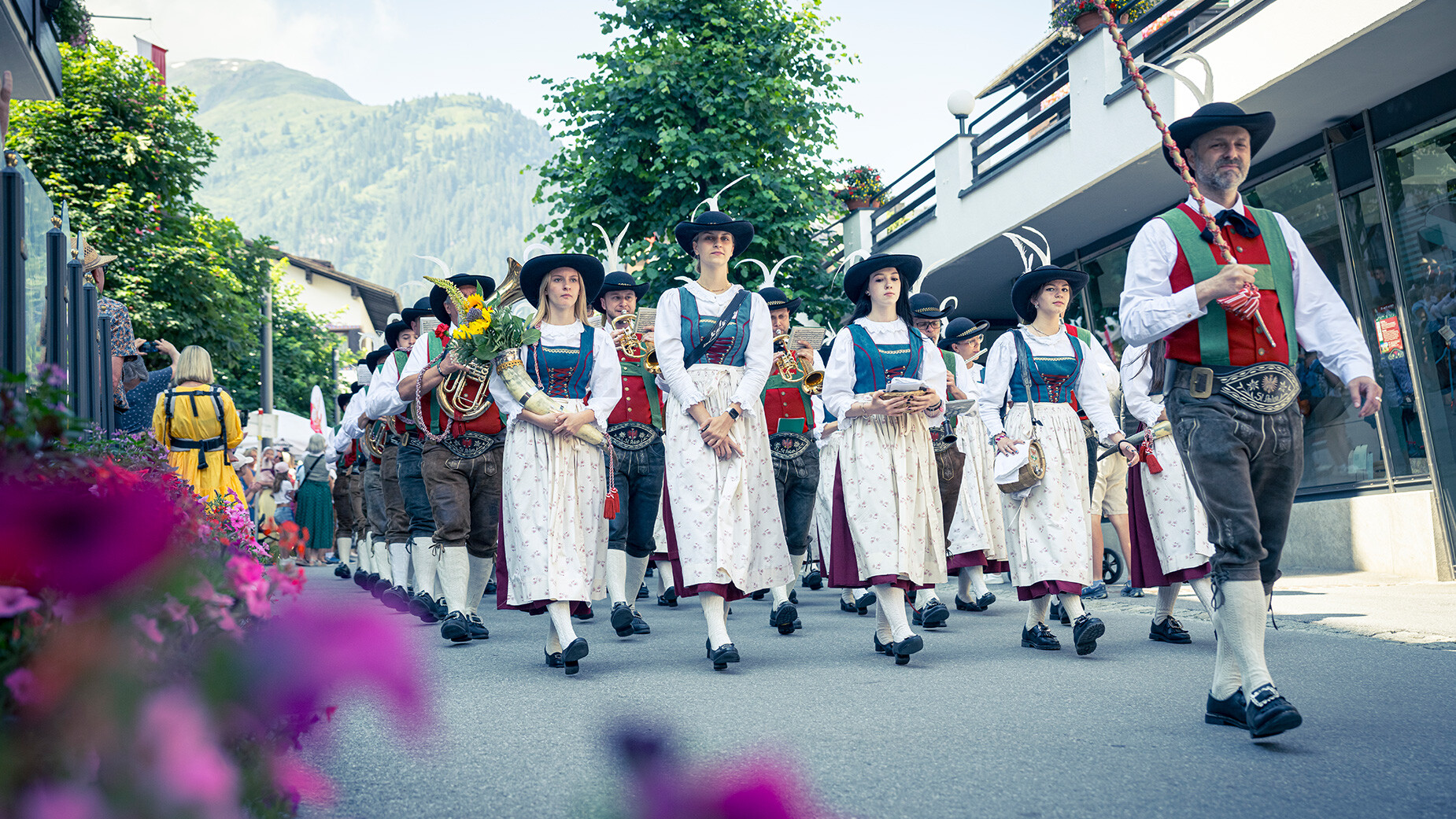 Frauen und Männer in traditioneller Tracht marschieren bei einem Festumzug durch die Straße / Women and men in traditional costumes parade through the street during a festival