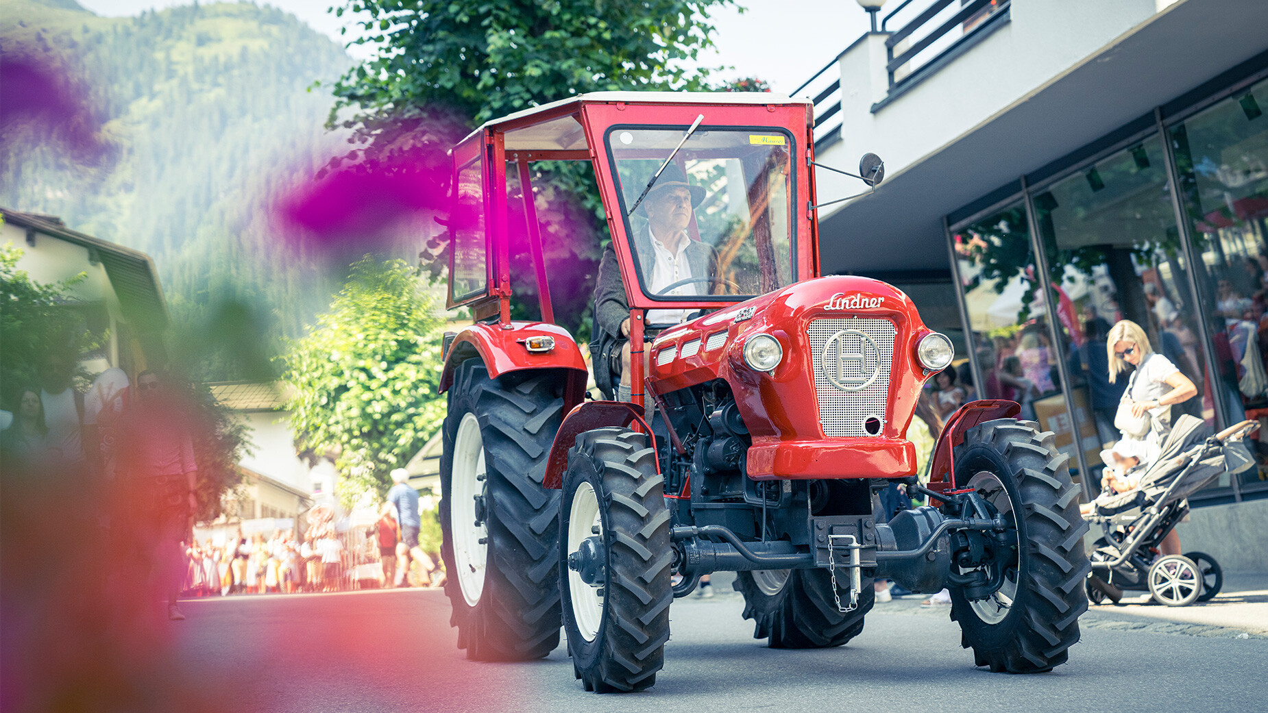 Roter Oldtimer-Traktor fährt durch das Dorf beim Festumzug, umgeben von Blumen / Red vintage tractor drives through the village during the parade, surrounded by flowers
