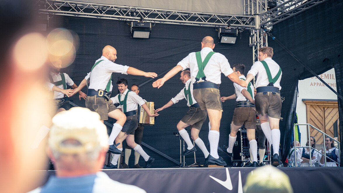 Gruppe in Lederhosen führt einen traditionellen Schuhplattler-Tanz auf einer Bühne auf / Group in lederhosen performs a traditional Schuhplattler dance on stage