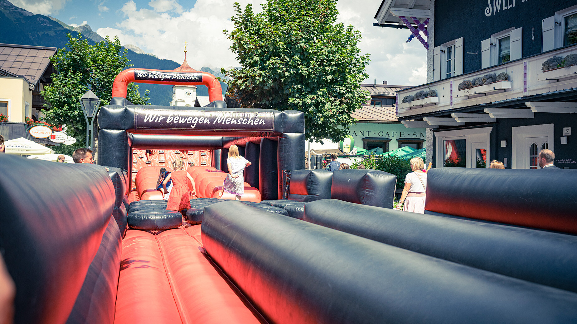 Kinder spielen auf einer rot-schwarzen Hüpfburg bei einem Sommerfest im Ort / Children play on a red and black bouncy castle during a local summer festival