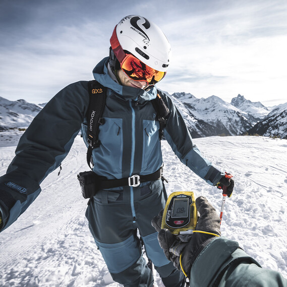 Ein Skifahrer bei Lawinensicherheitstraining mit LVS-Gerät vor alpiner Winterkulisse.