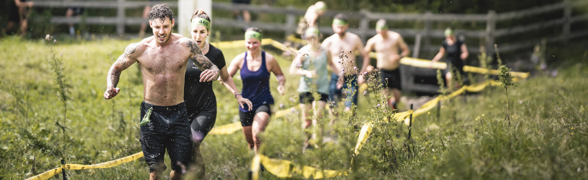 Teilnehmer beim Wadlbeisser-Hindernislauf sprinten durch Schlamm und Wiesen – Kraft, Ausdauer und Spaß in der Natur.
