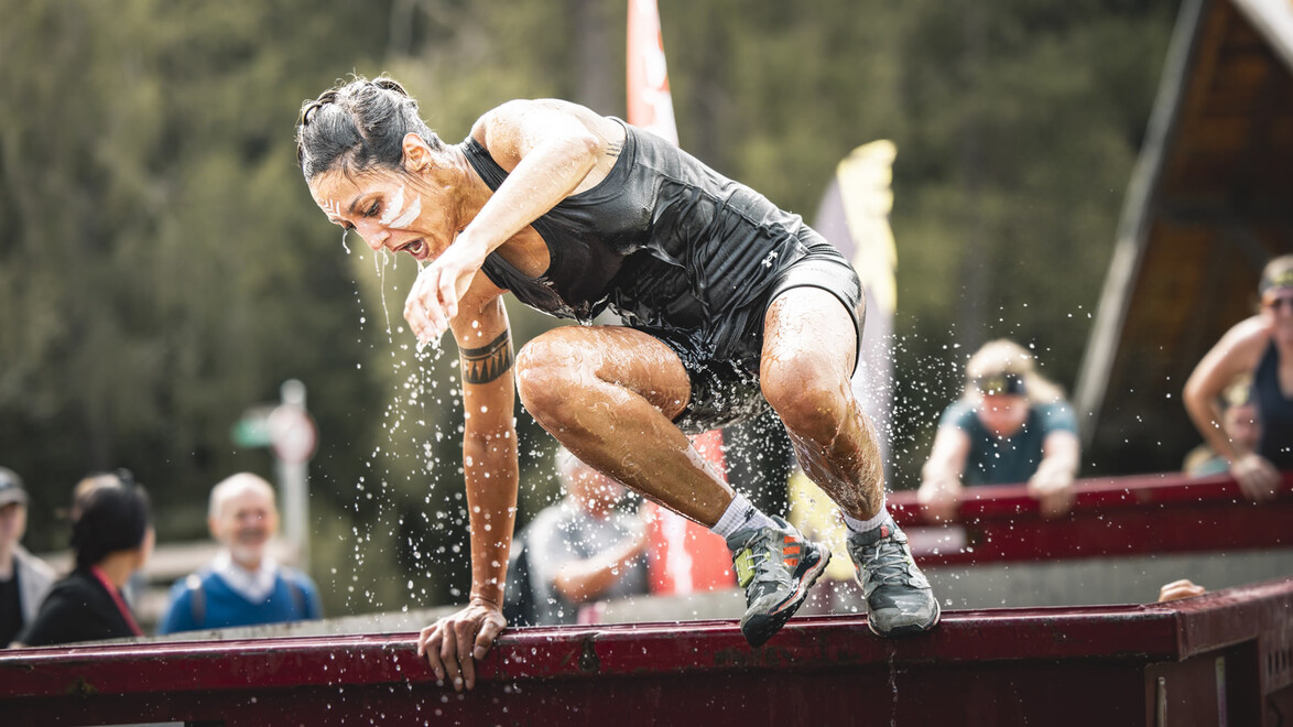 Eine Frau überquert ein nasses Hindernis bei einem Hindernislauf im Freien. / A woman crosses a wet obstacle during an outdoor obstacle race
