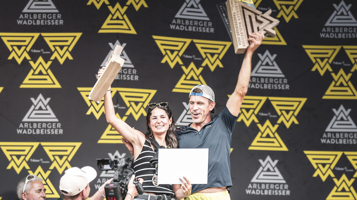 Zwei Sieger:innen feiern mit Trophäen auf der Bühne des Arlberger Wadlbeißers. / Two winners celebrate with trophies on the Arlberger Wadlbeißer stage.