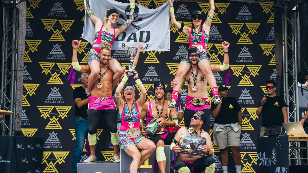Ein verkleidetes Team posiert jubelnd auf der Siegerbühne nach dem Lauf. / A costumed team poses cheering on the winner's stage after the run.