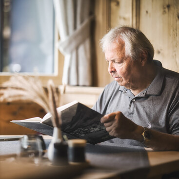 Andreas Fahrner liest konzentriert in einem Dialektbuch, während er an einem Tisch in einer gemütlichen, holzgetäfelten Stube sitzt.