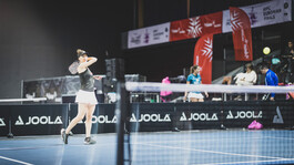  Frau beim Aufschlag bei einem Pickleball-Match in einer Halle mit Turnierbannern