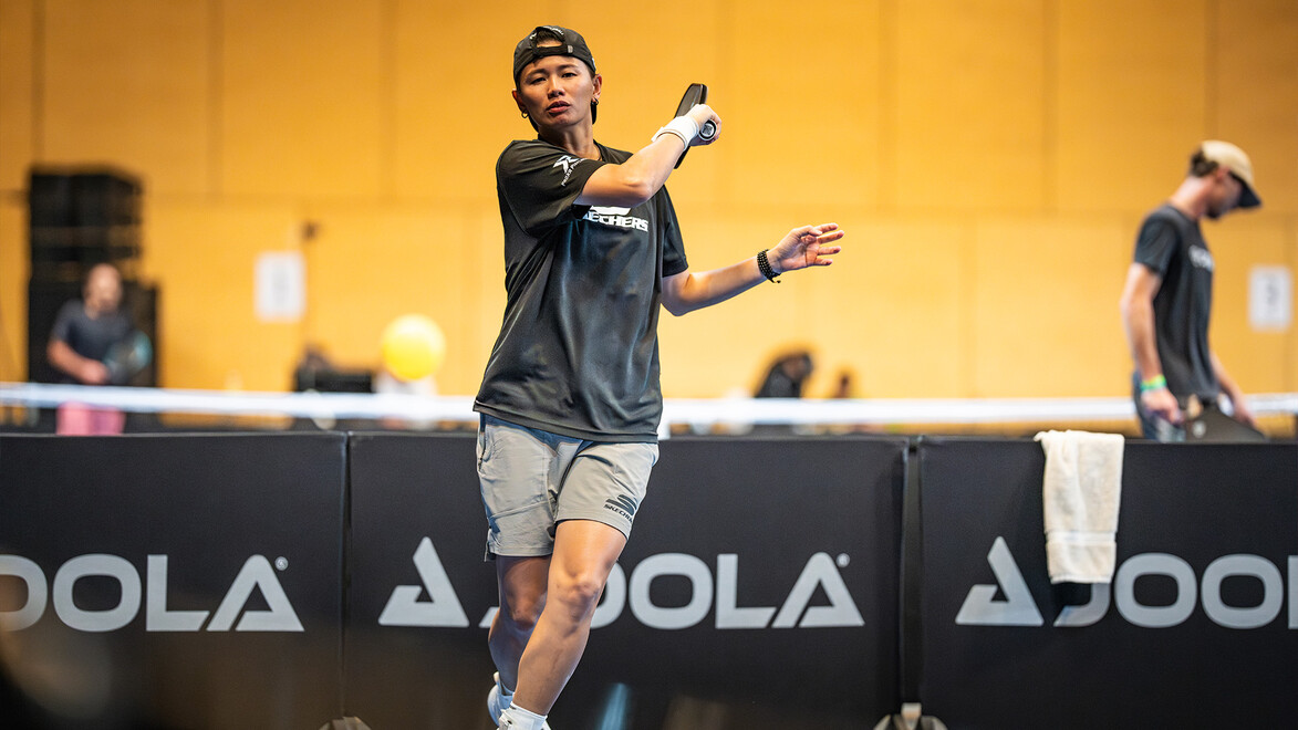 Ein Spieler fokussiert sich auf den Ball während des Spiels, im Hintergrund weitere Teilnehmer beim Warm-up / A player focuses on the ball during the match, with others warming up in the background
