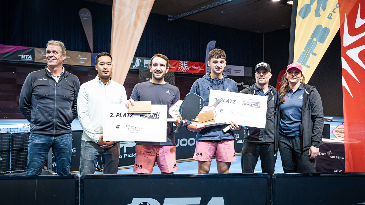 Gruppe von Siegern mit Pokalen und Schecks auf dem Siegerpodest, begleitet von Organisatoren / Group of winners with trophies and checks on the podium, accompanied by organizers