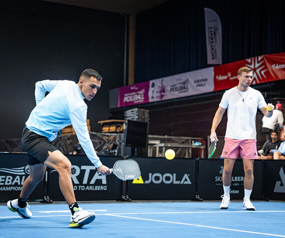 Zwei Pickleballspieler beim Aufwärmen auf dem blauen Teppichboden, in der Multifunktionshalle im Arlberg WellCom - der WM-Halle.