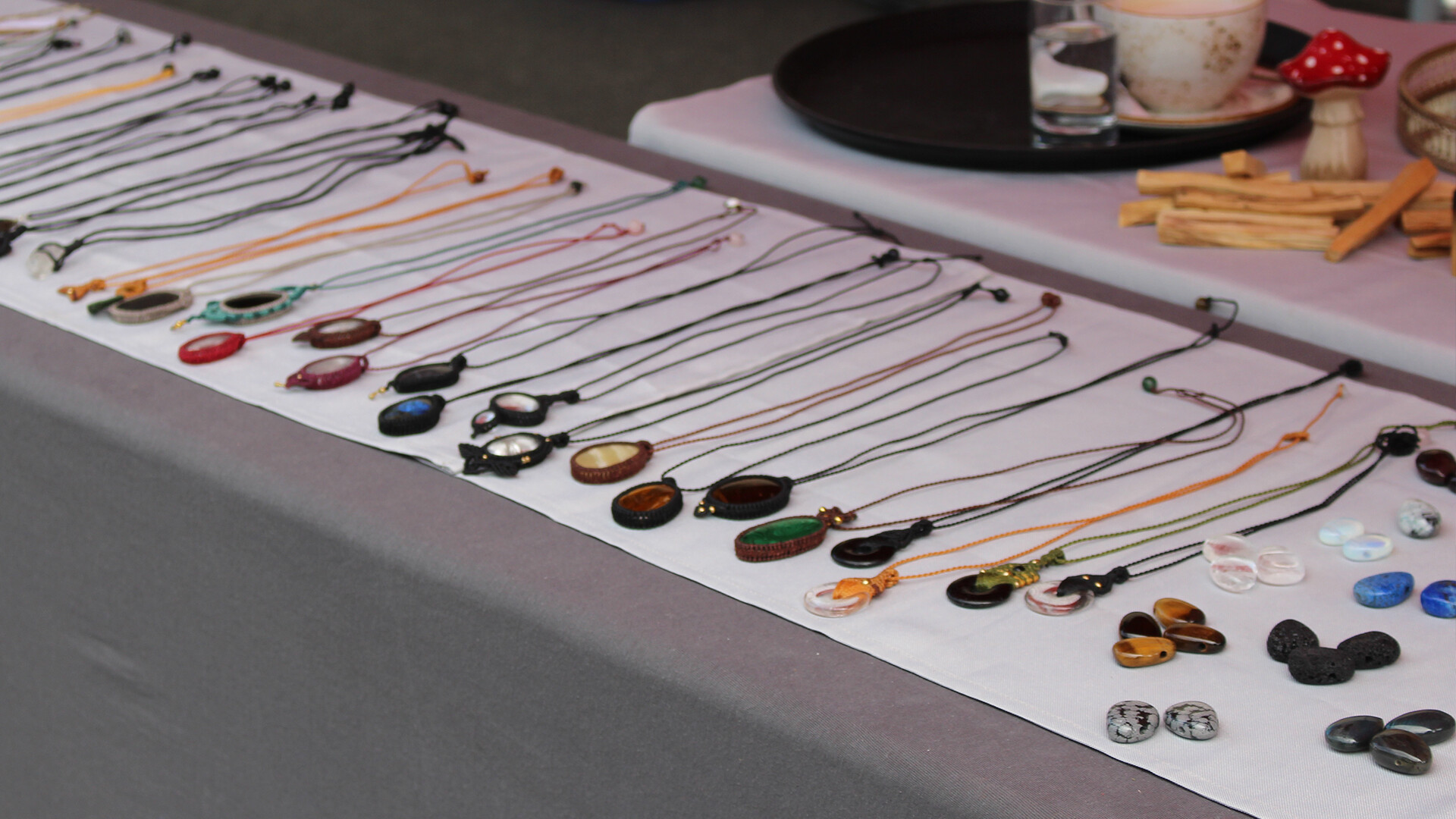 Bunte Ketten, Anhänger und Ringe ordentlich auf einem weißen Tisch ausgebreitet. / Colorful necklaces, pendants and rings neatly spread on a white table.