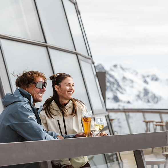 Paar genießt Bier und Wein auf einer Terrasse (Rendl-Beach) mit Alpenblick.
