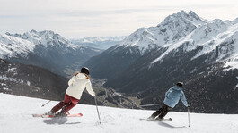 Frühjahrsskitag in den Alpen – Zwei Skifahrer genießen die perfekte Abfahrt mit atemberaubendem Bergpanorama
