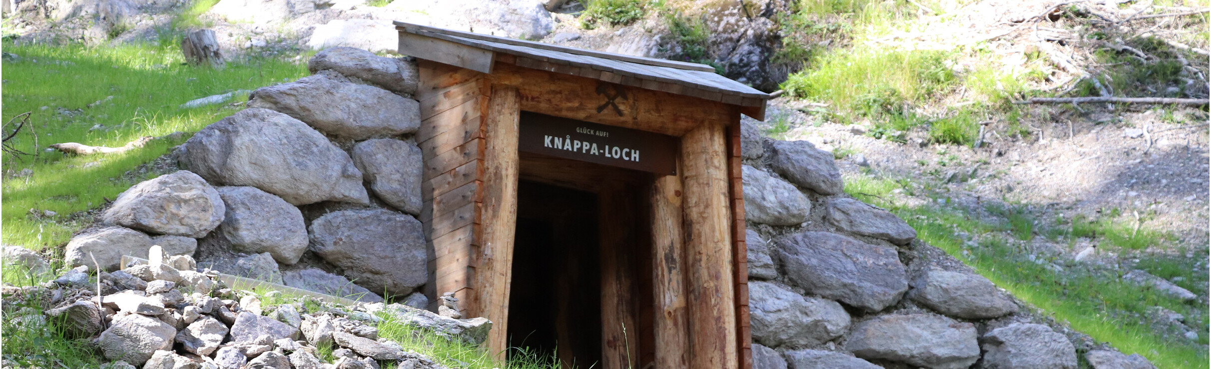 Historische tunnelingang naar het zogenaamde "Knappa Loch" in het bos met informatiepaneel en houten bank bij St. Anton am Arlberg.