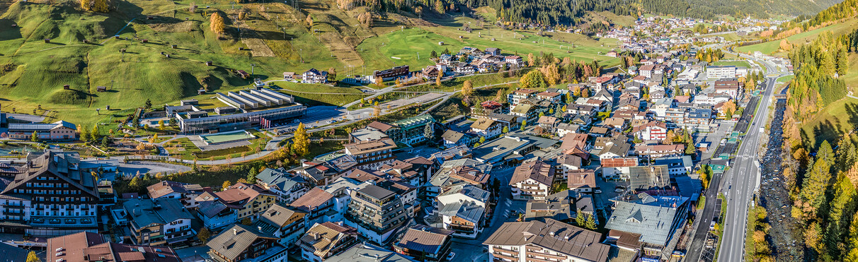 Aerial view of St. Anton am Arlberg in autumn with valley, houses and green slopes.