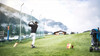 Golfen in St. Anton am Arlberg Golfer schlägt auf grünem Fairway ab, dahinter Berge, Nebel und ein kleines Clubhaus.