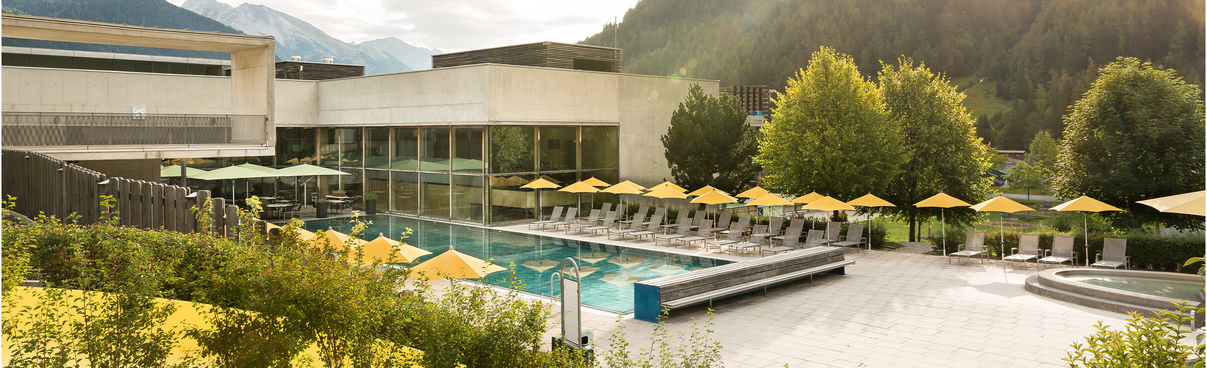 Das Außenbecken des Arlberg WellCom mit gelben Sonnenschirmen und Bergblick im Hintergrund.