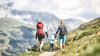 Familie wandert gemeinsam einen alpinen Weg mit blühenden Wiesen und Bergkulisse / Family hikes along an alpine trail with blooming meadows and mountain scenery