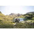 Drei Wanderer rasten an einem kleinen See mit Blick auf die schroffen Berge des Arlbergs / Two hikers rest by a small alpine lake with rugged Arlberg mountains in the background