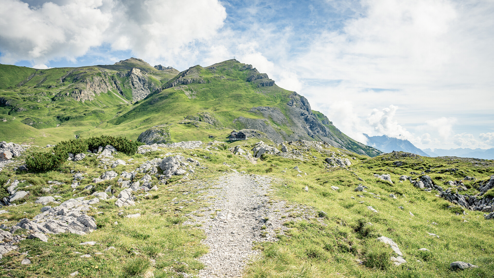 Ein schmaler Wanderpfad führt durch grüne Almwiesen hinauf zu einem aussichtsreichen Bergrücken / A narrow hiking trail leads through green alpine meadows to a scenic ridge
