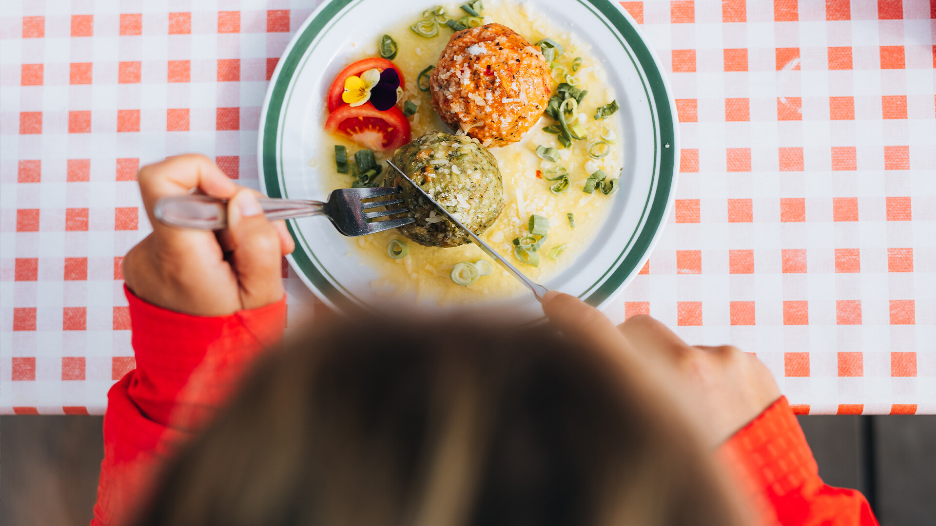 Eine Person isst auf kariertem Tischtuch ein traditionelles Gericht mit Knödeln und Soße / A person enjoys a traditional dish with dumplings and sauce on a checkered tablecloth