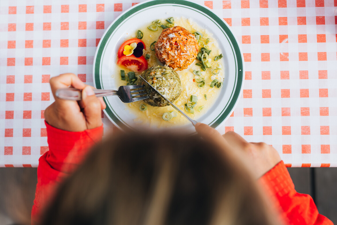 Eine Person isst auf kariertem Tischtuch ein traditionelles Gericht mit Knödeln und Soße / A person enjoys a traditional dish with dumplings and sauce on a checkered tablecloth