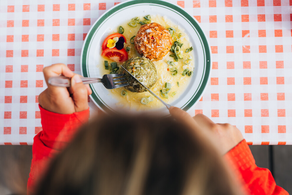 Eine Person isst auf kariertem Tischtuch ein traditionelles Gericht mit Knödeln und Soße / A person enjoys a traditional dish with dumplings and sauce on a checkered tablecloth