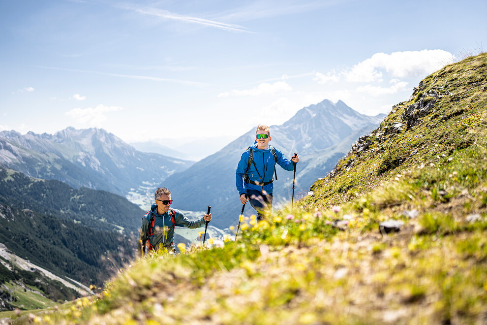 Zwei Wanderer mit Stöcken steigen einen steilen Hang mit Blick ins Tal hinauf / Two hikers with poles ascend a steep slope with a wide view into the valley