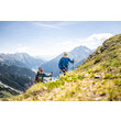 Zwei Wanderer mit Stöcken steigen einen steilen Hang mit Blick ins Tal hinauf / Two hikers with poles ascend a steep slope with a wide view into the valley