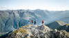 Gruppe steht am Gipfel mit Panorama auf Berglandschaft und Tal von St. Anton am Arlberg / Group stands on a summit with panoramic views of the mountain landscape and St. Anton valley