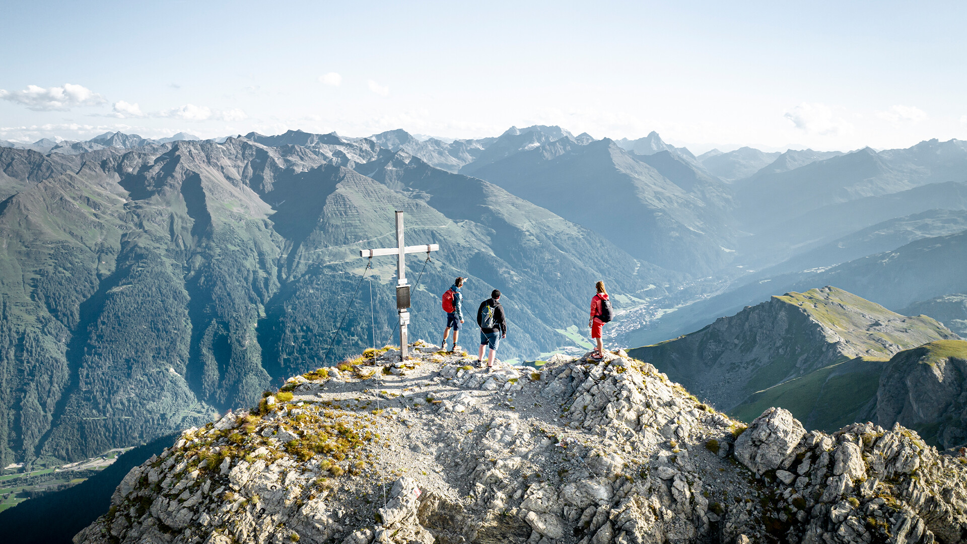 Gruppe steht am Gipfel mit Panorama auf Berglandschaft und Tal von St. Anton am Arlberg / Group stands on a summit with panoramic views of the mountain landscape and St. Anton valley