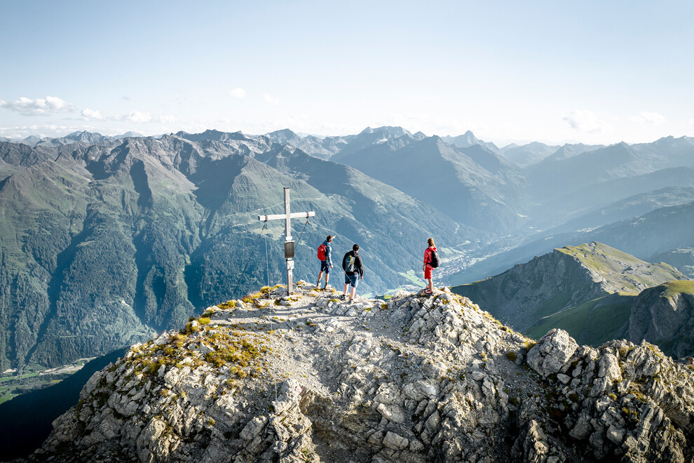 Gruppe steht am Gipfel mit Panorama auf Berglandschaft und Tal von St. Anton am Arlberg / Group stands on a summit with panoramic views of the mountain landscape and St. Anton valley