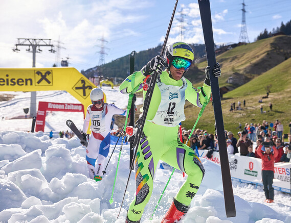 Dieter steigt mit Skiern über die Schneehügel Richtung Ziel dicht gefolgt von Dominik Schranz.