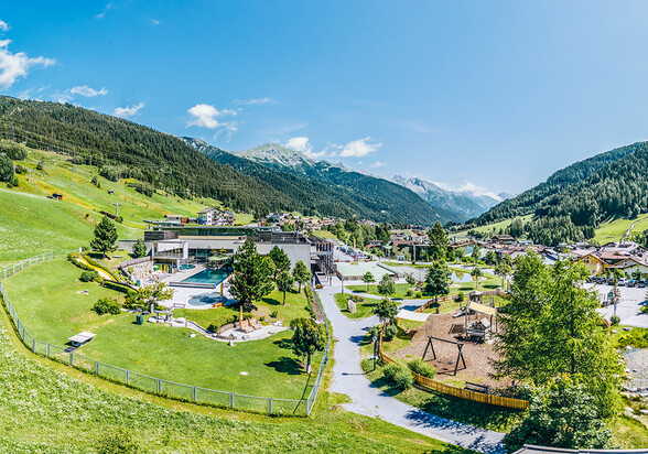 Panoramablick auf das Sommerdorf St. Anton mit Freibad, Spielplatz und Bergkulisse.