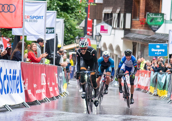 Radrennfahrer im Zielsprint des Arlberg Giro durch die Dorfstraße von St. Anton, umgeben von jubelnden Zuschauer:innen.