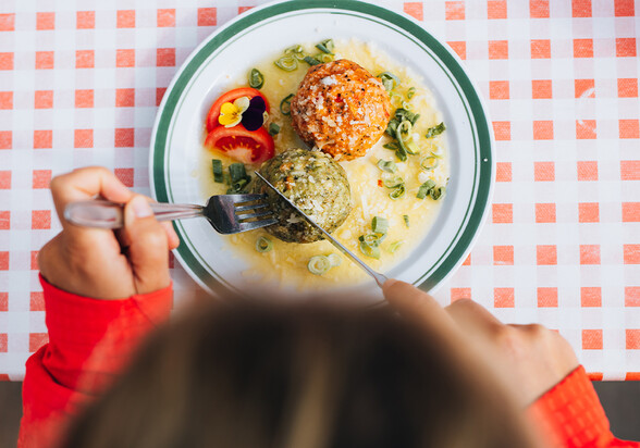 Zwei Knödel mit Soße und Blüten auf weißem Teller, von Person mit Messer und Gabel angeschnitten.
