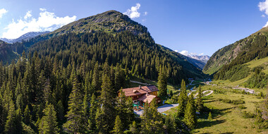 The Konstanzer Hütte is idyllically situated in the middle of a green Alpine valley with dense forests, striking mountains and a clear sky.