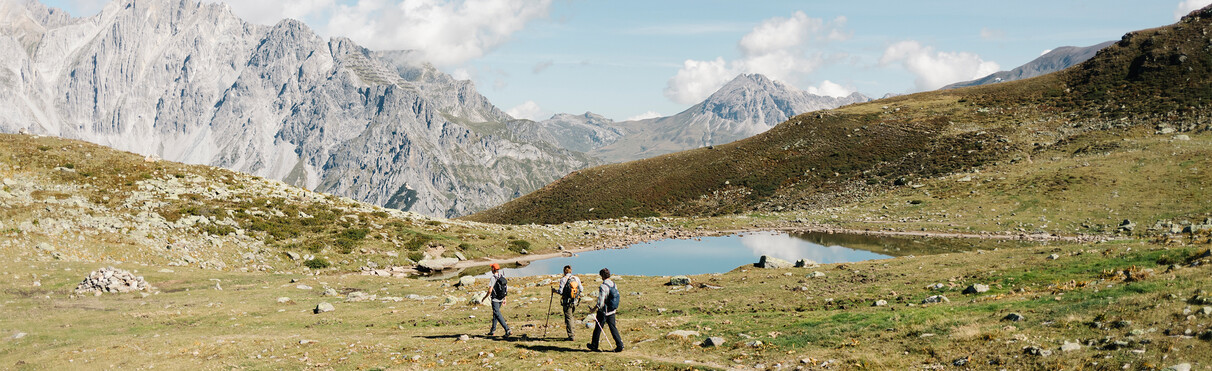 Drei Wanderer auf einem Hochplateau am gehen, im Hintergrund sind rustikale Bergfronten zu sehen.